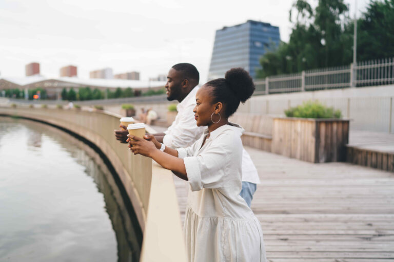 Cheerful black couple with coffee standing on promenade